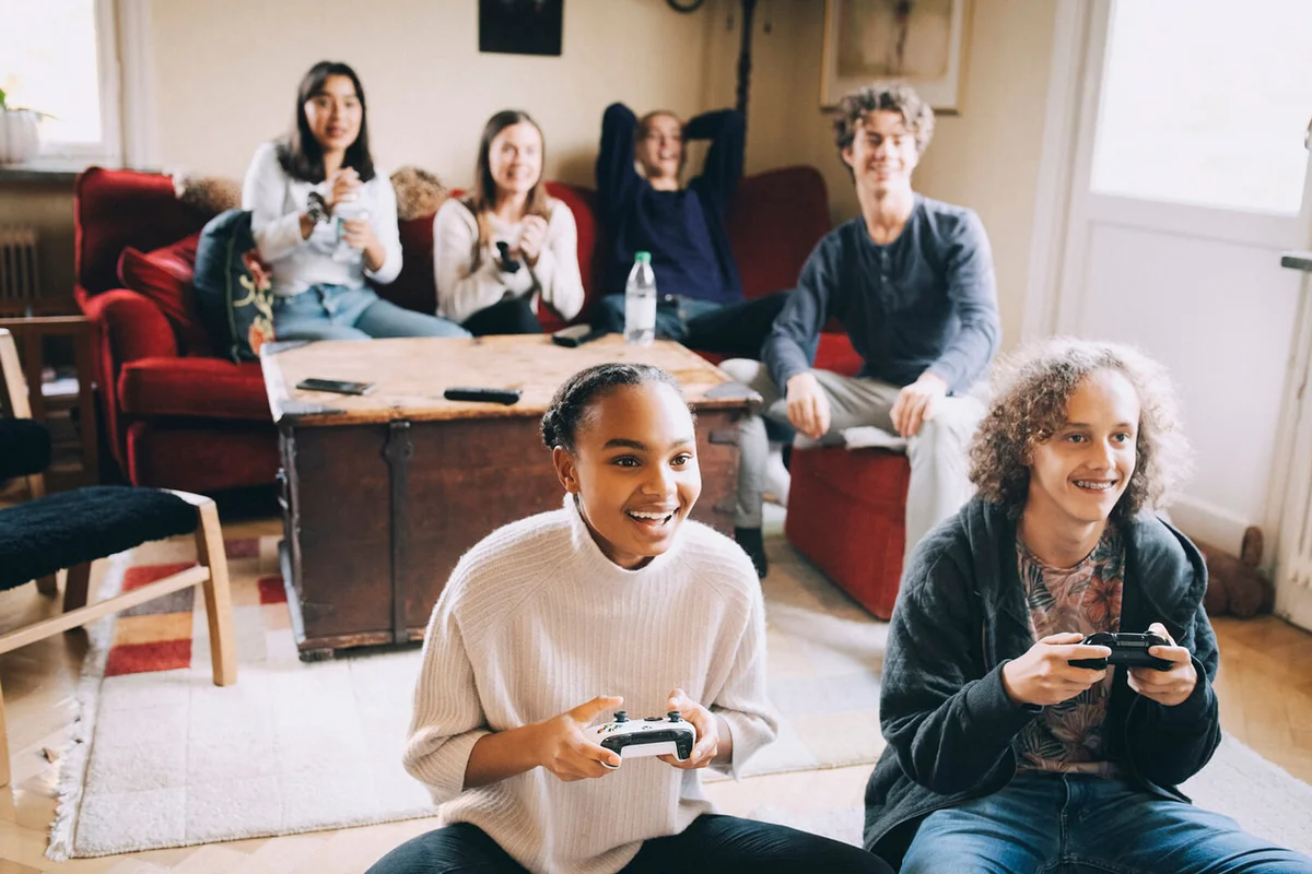 Happy teenagers playing video game while friends sitting on sofa in living room