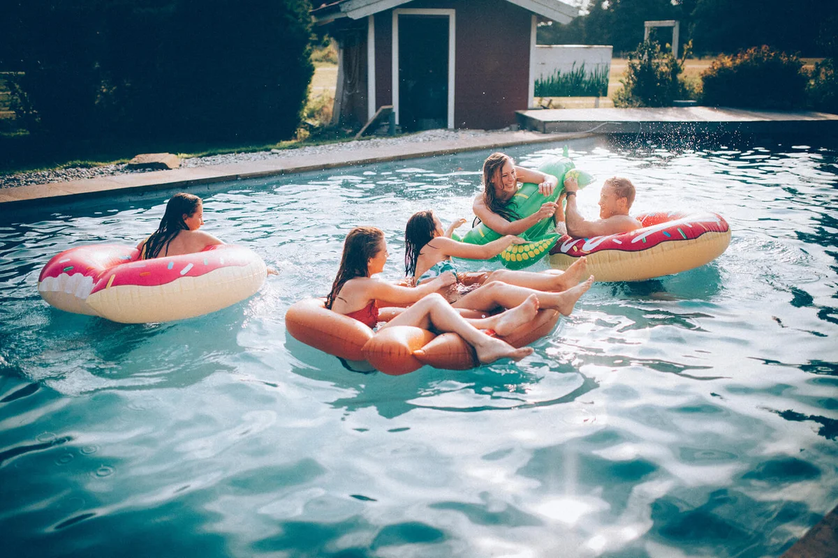 Friends playfully fighting in a pool with inflatable floats