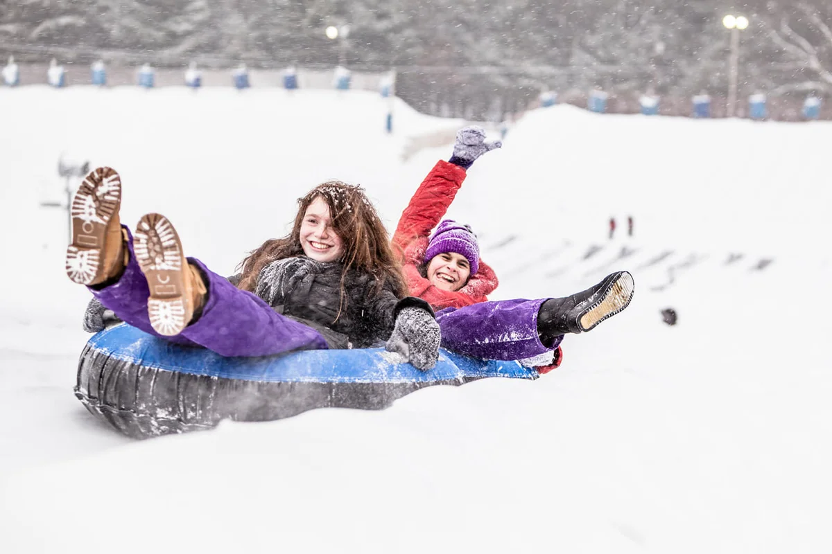 Two sisters, teenager girl and little girl, have fun with snowtubing at the winter resort