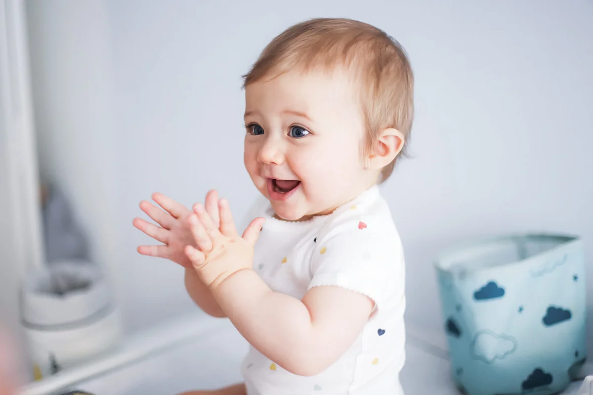 A 1 year old baby girl clapping her hands on her baby-changing table