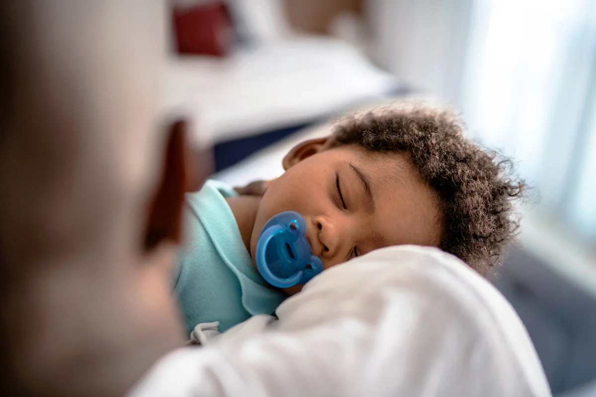 Father putting baby son to sleep on his arms at home