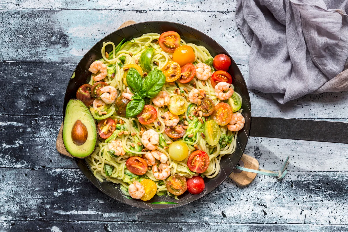 Frying pan of spaghetti with zoodles, guacamole, tomatoes and shrimps