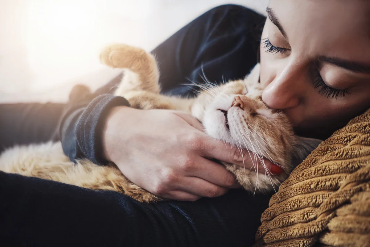 Woman kisses her cat while they sleep cuddling on the sofa