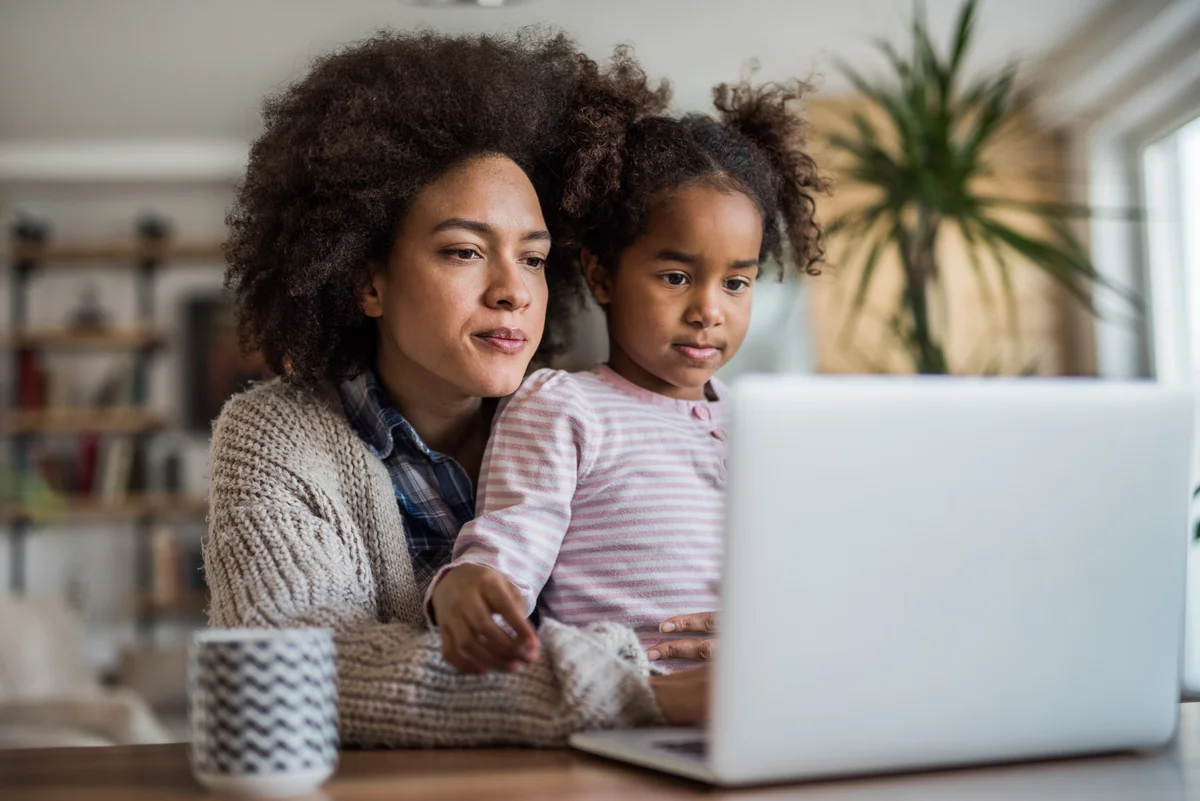 mother and young daughter watching online memorial on laptop