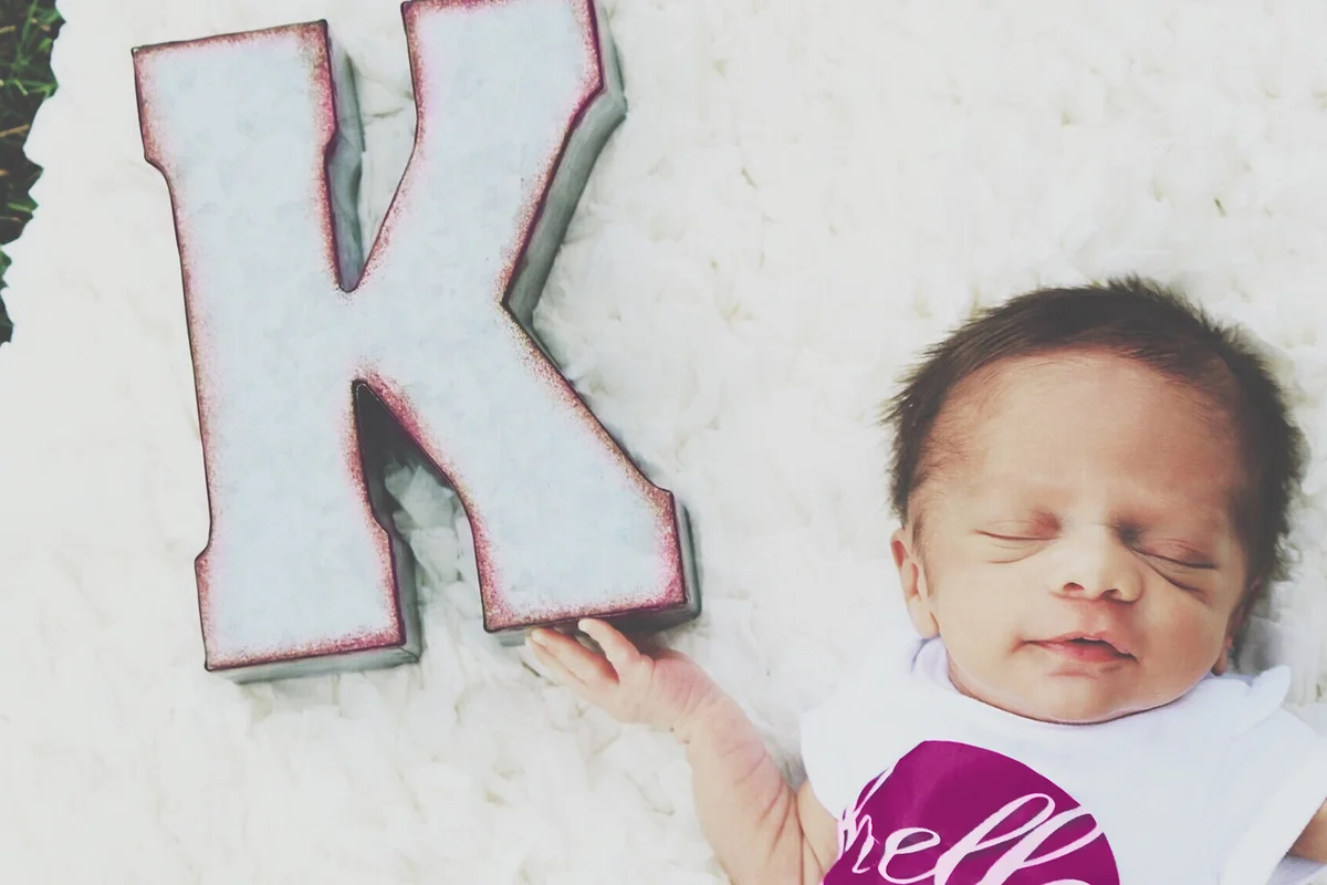 Directly Above Shot Of Baby Girl Sleeping By Letter K On Rug