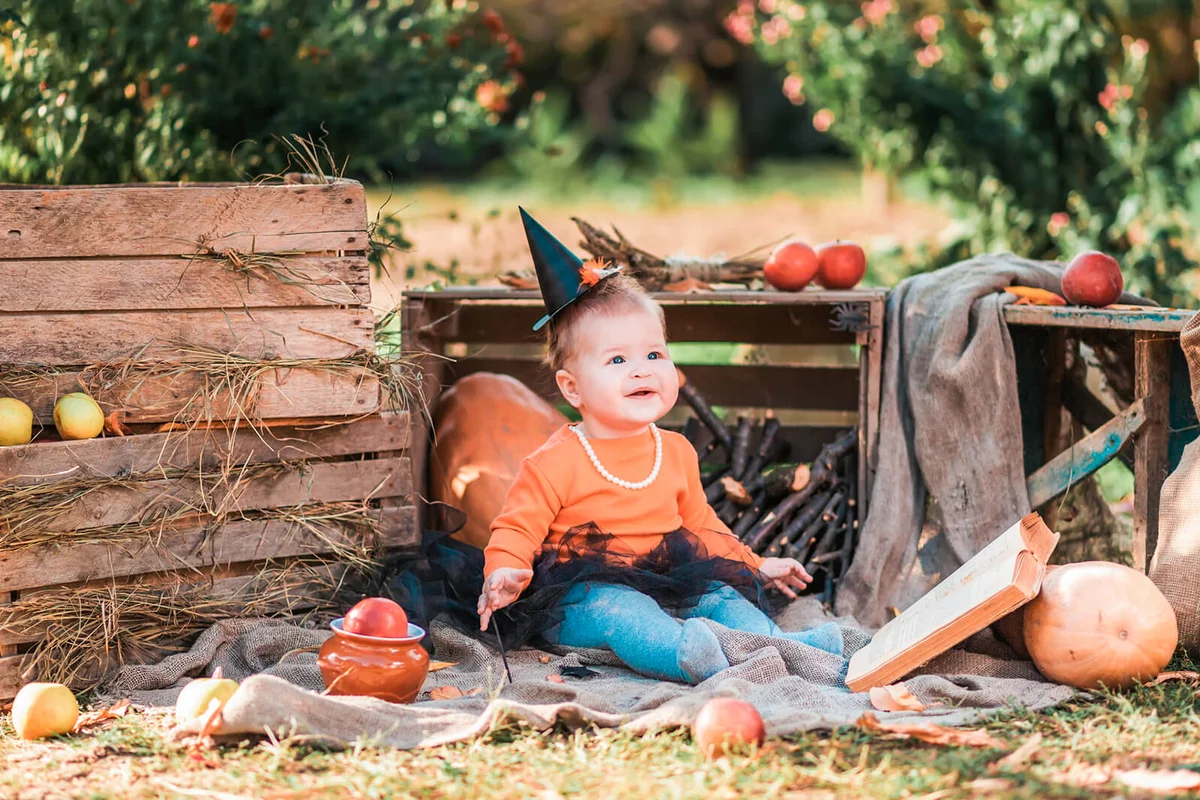 A happy baby girl in a witch costume sitting in kitchen-garden