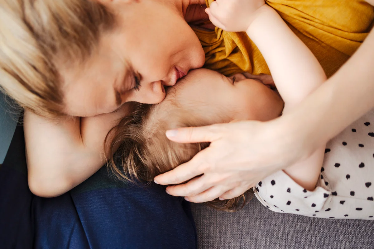 Mother Kissing Her Sleepy Little Daughter on Sofa