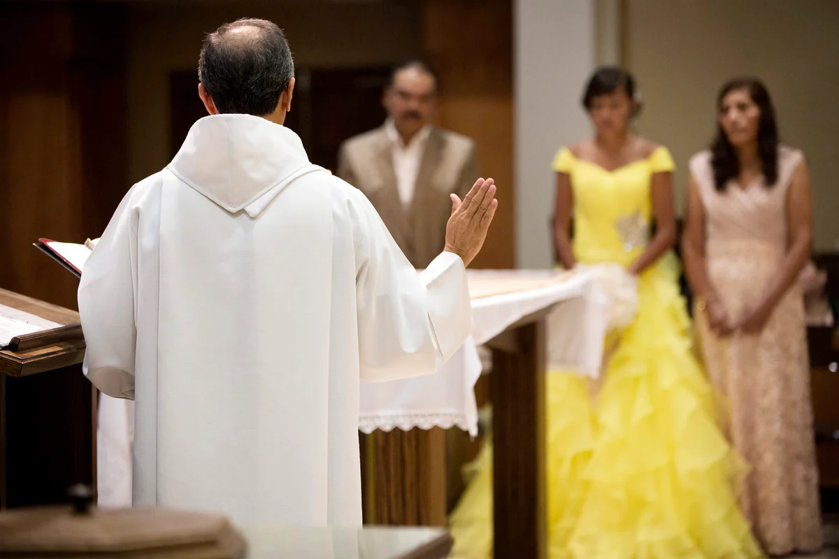 Hispanic family celebrating quinceanera with priest in Catholic church