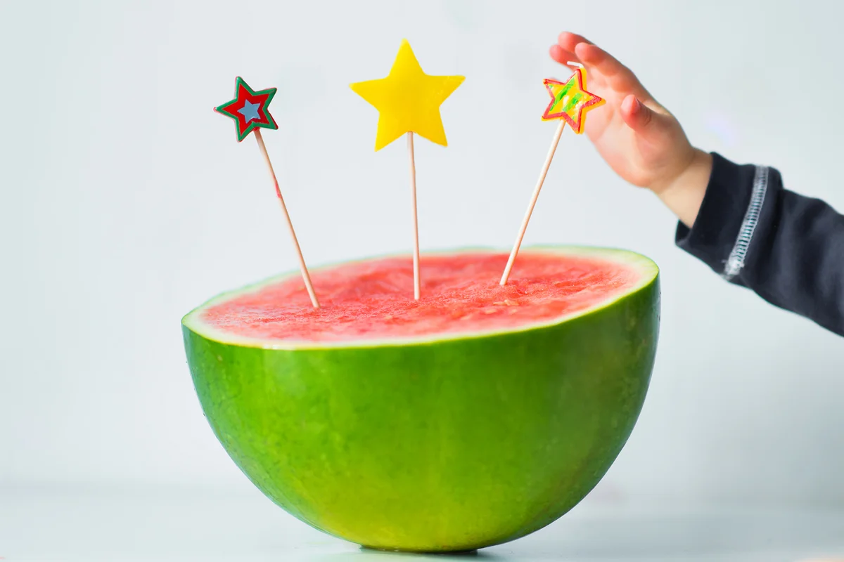Baby hand putting candle in watermelon birthday cake