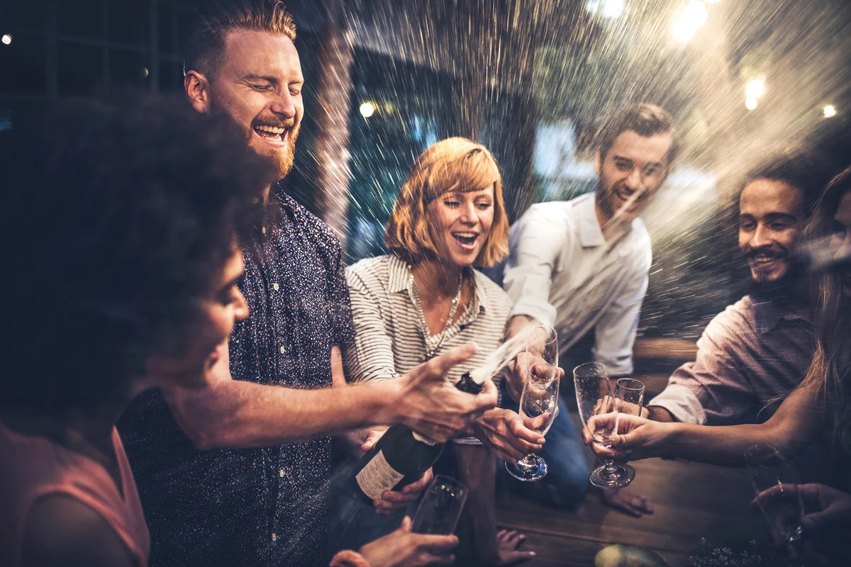 man opening a champagne on a party with his friends