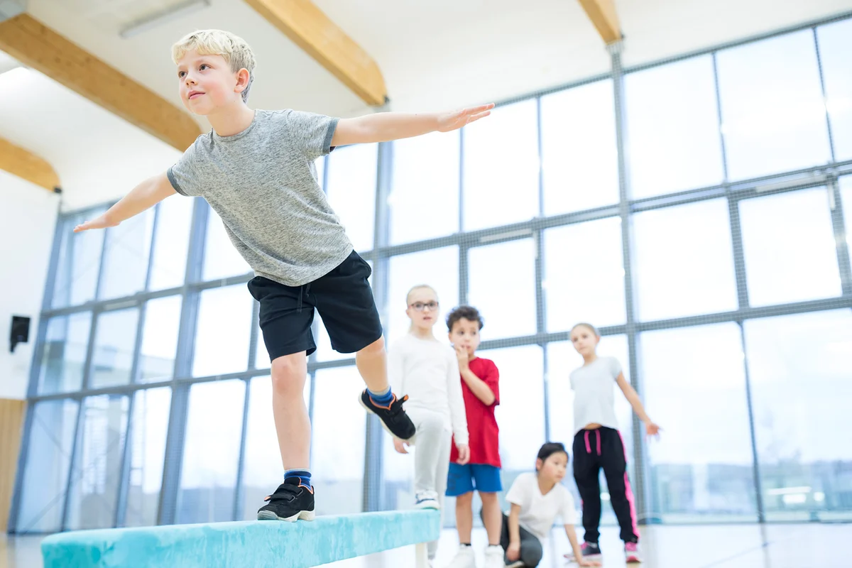 Schoolboy balancing on balance beam in gym center