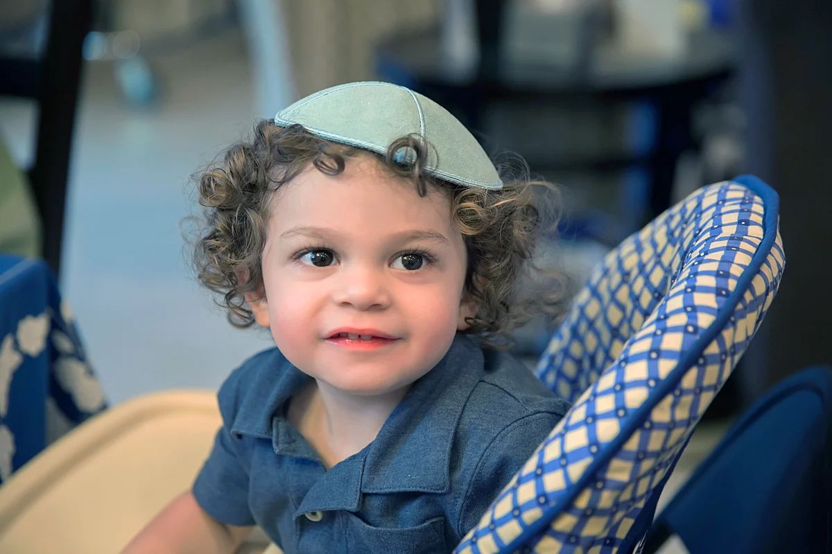 Little boy wearing a yarmulke sits in highchair