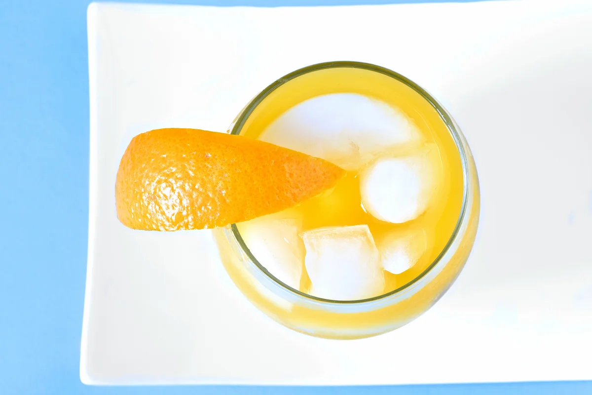 Overhead image of a glass of orange juice with ice and orange wedge