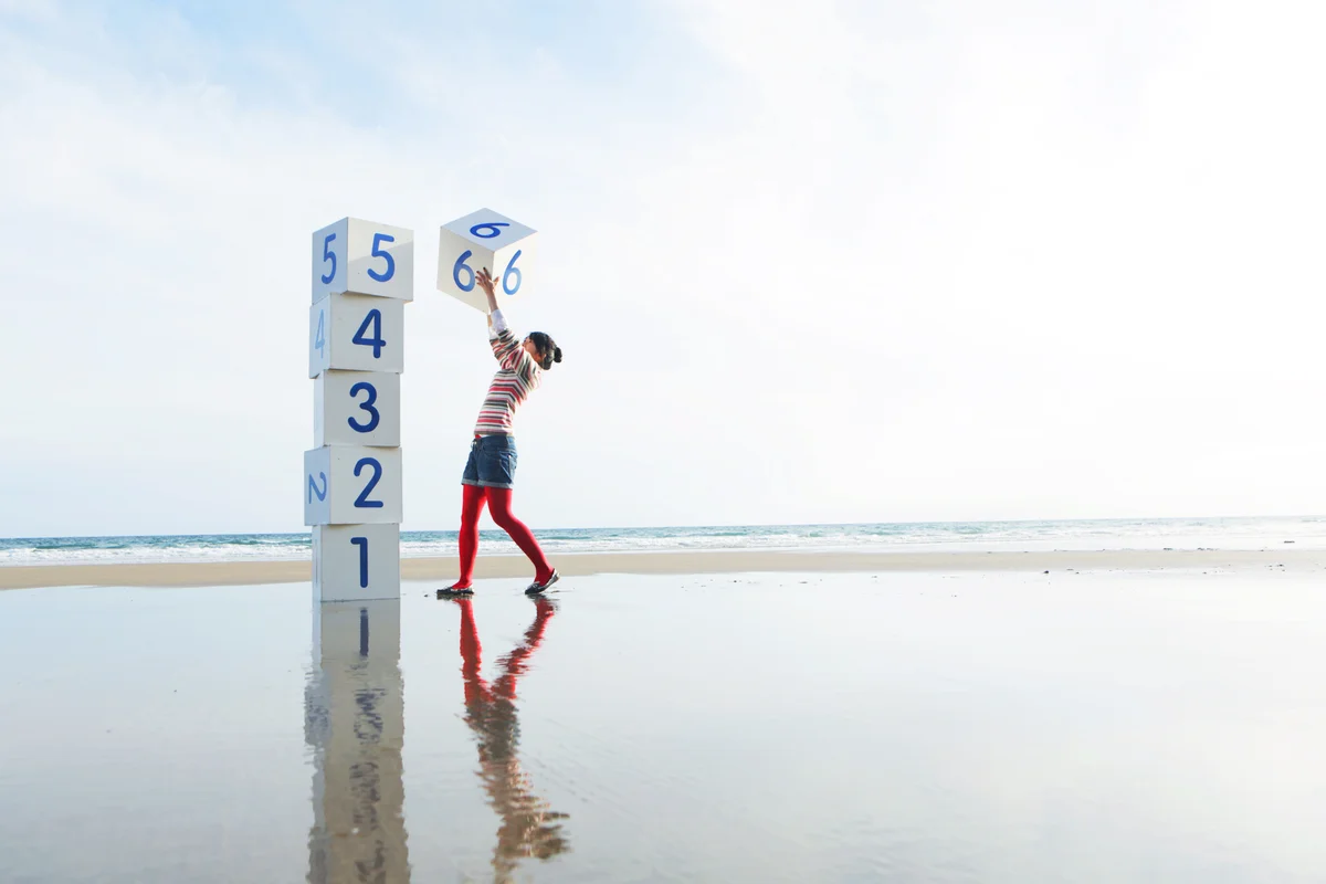 Girl on beach stacking numbered boxes