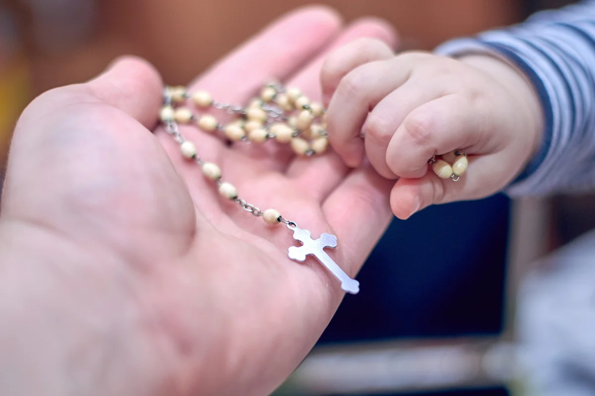 Small child takes a rosary from his dad's hand