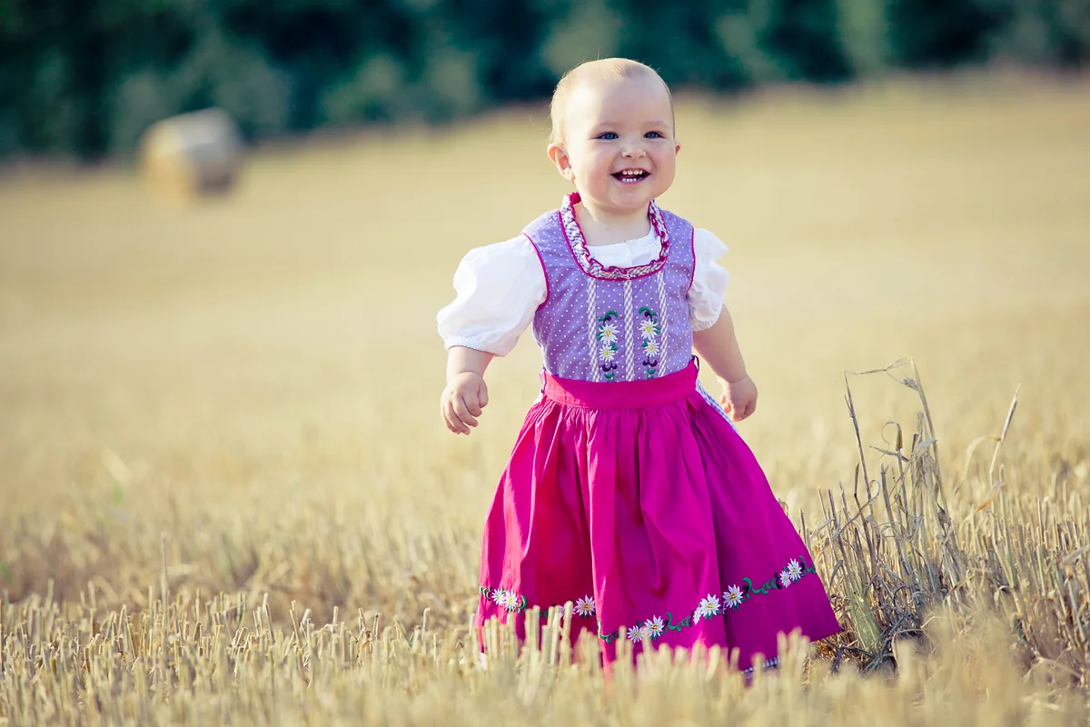 Baby girl with dirndl laughs on a stubble field