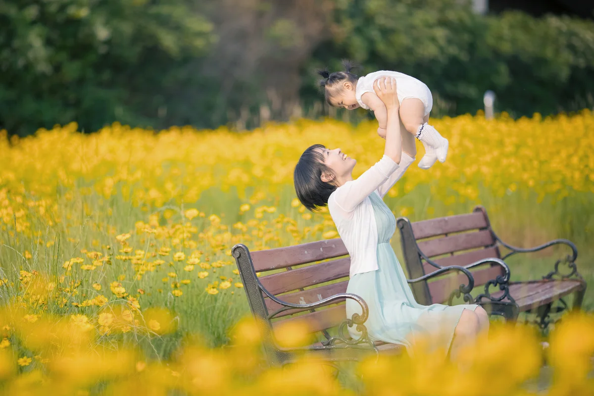 Mother playing with baby girl in yellow flower field
