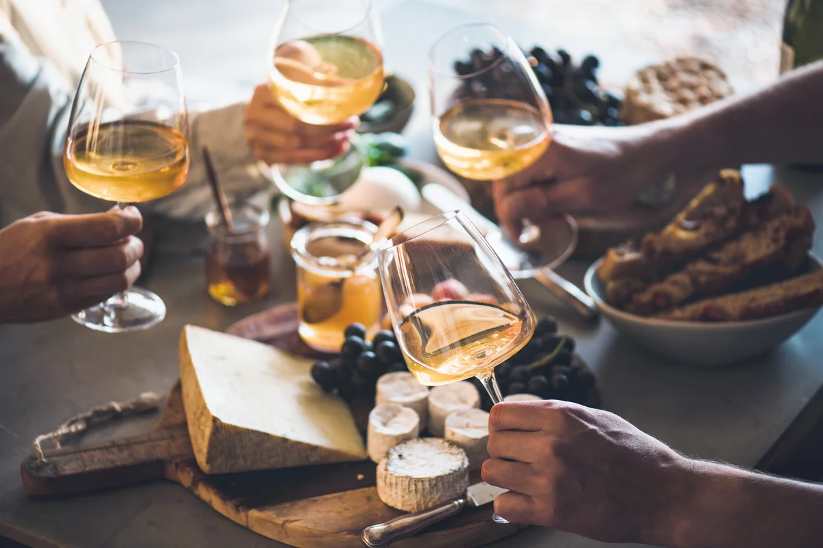 Hands of people holding wineglasses over a table of cheeses