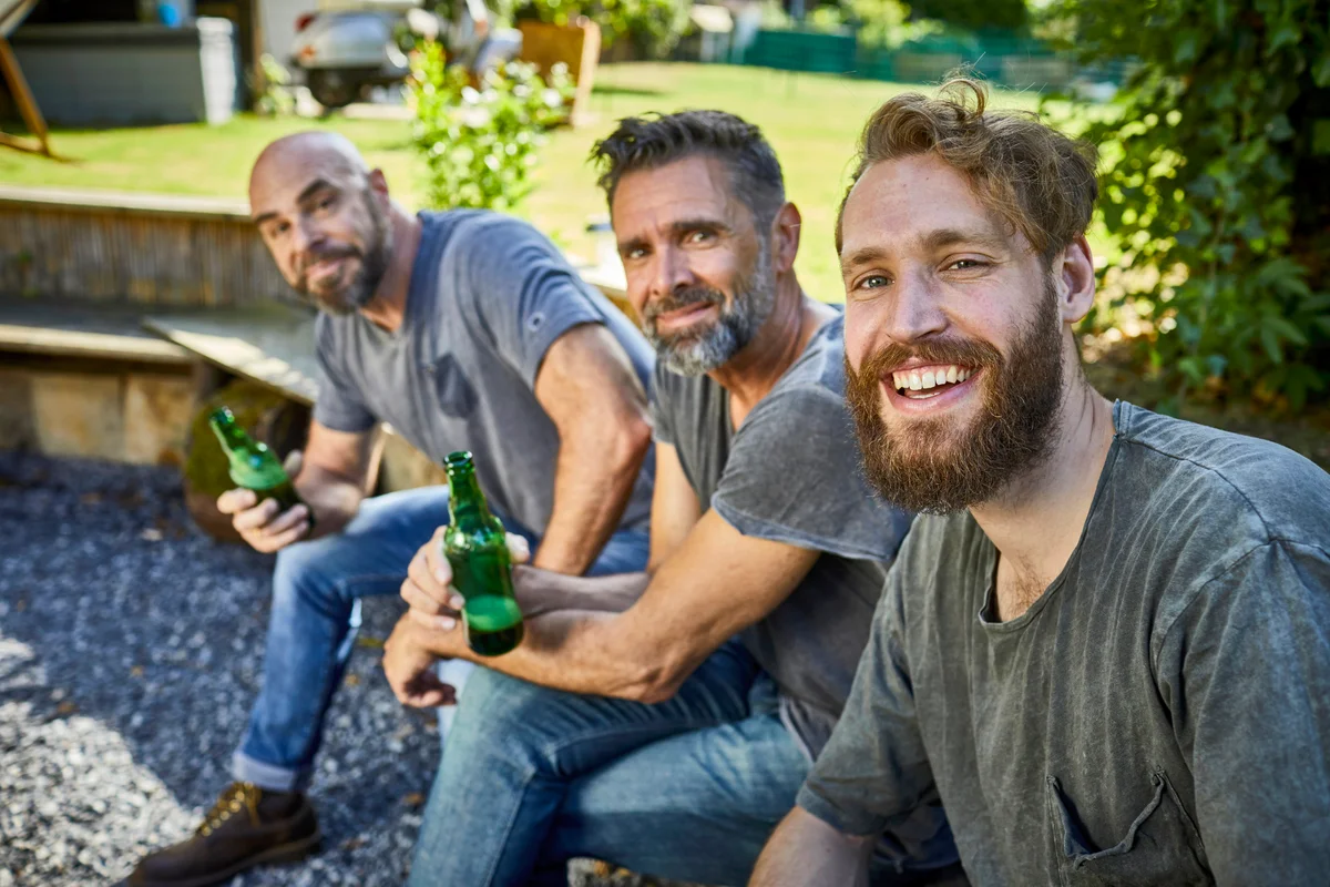 Happy friends sitting together with beer bottles in garden