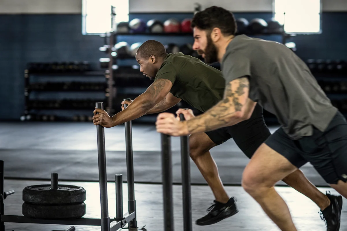 Men pushing weighted sled at cross training gym