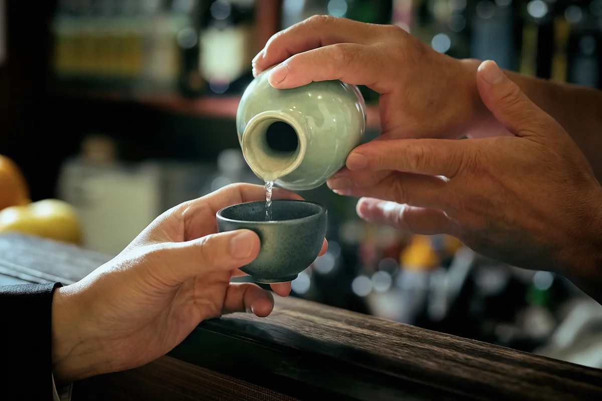 Close-up of bartender hand pouring Sake to glass which hands of adult man