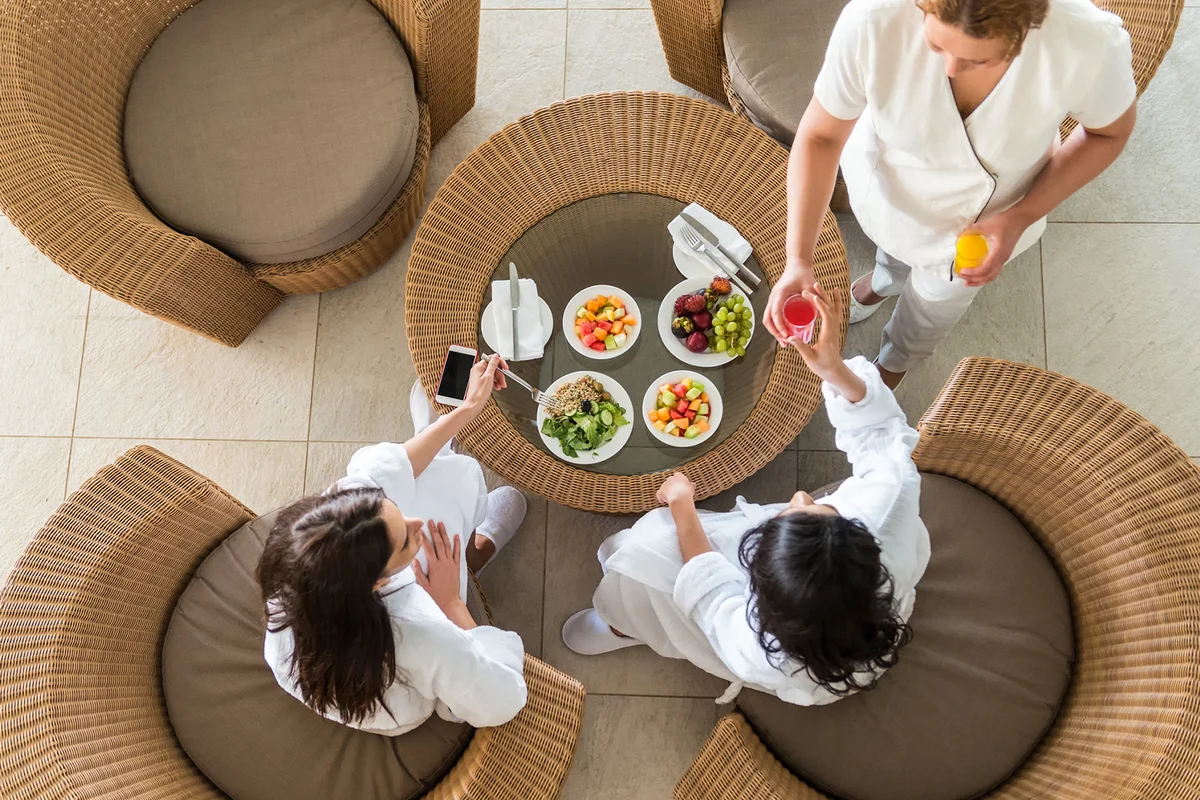 Two girlfriends in bathrobes and slippers eating a healthy spa lunch at a resort hotel