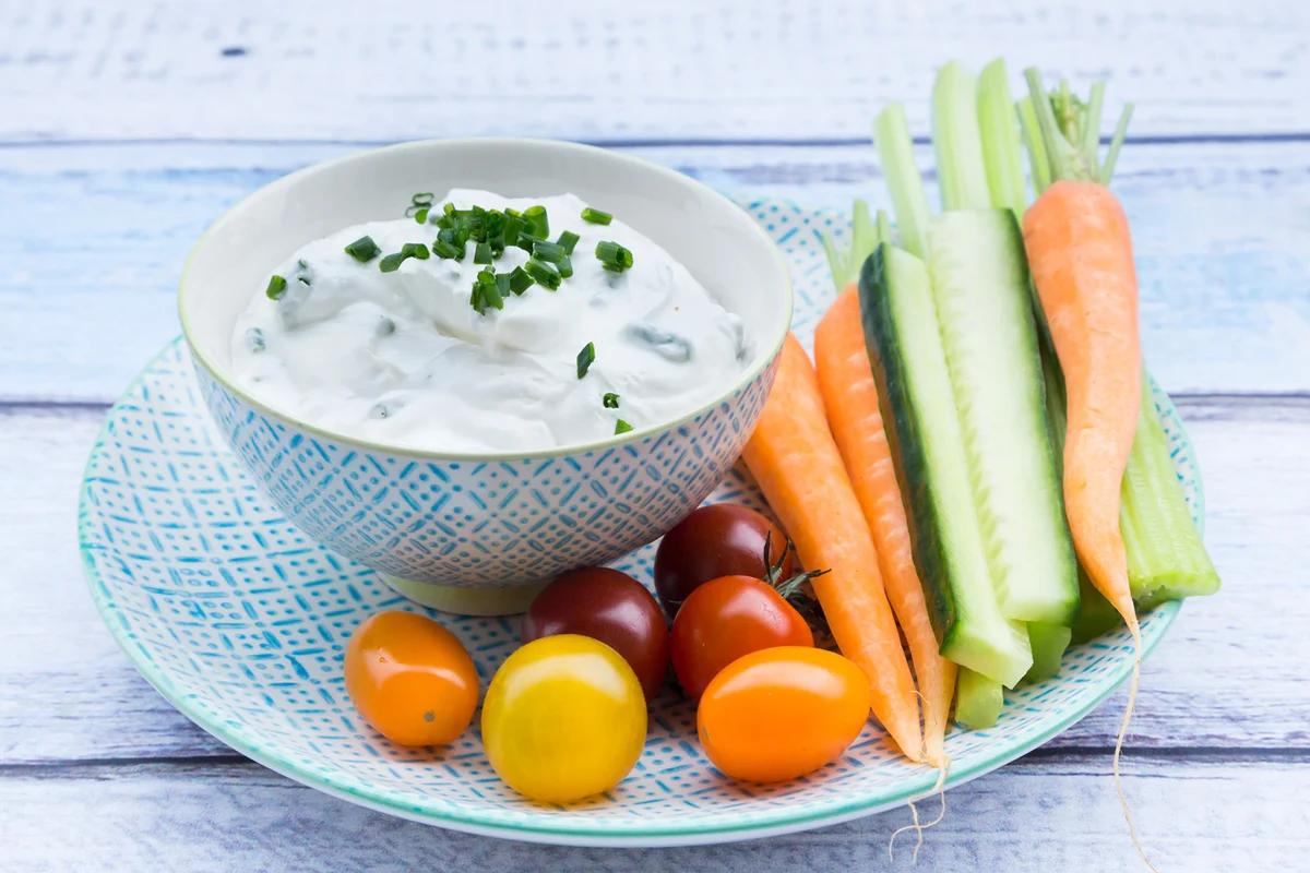 Bowl of dipping sauce, cherry tomatoes and vegetable sticks on plate
