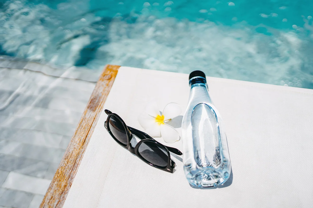 Water bottle, sunglasses and flower petal on a deck chair