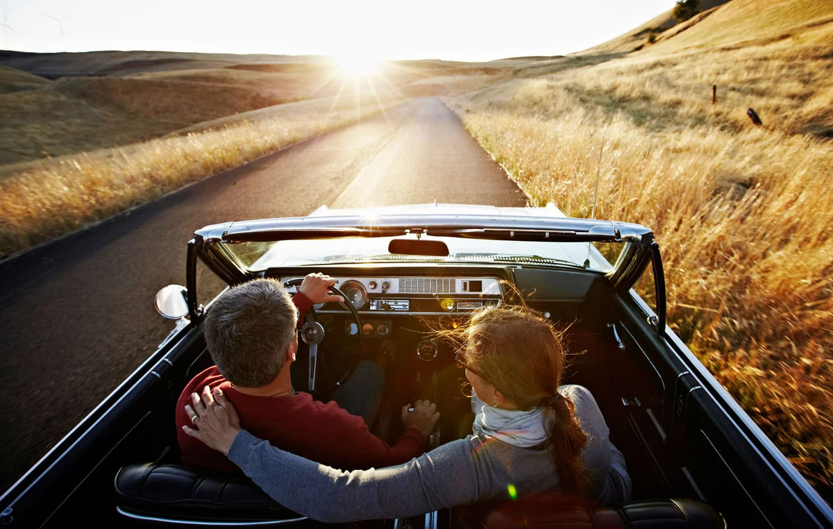 couple driving in convertible car sunset on horizon