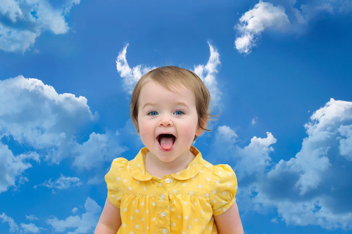 Baby girl in a yellow dress under cloud horns