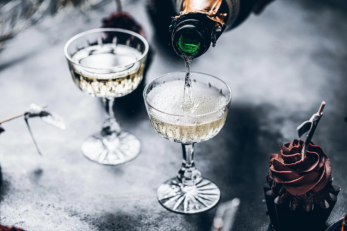 pouring prosecco in a glasses over black table with cup cake