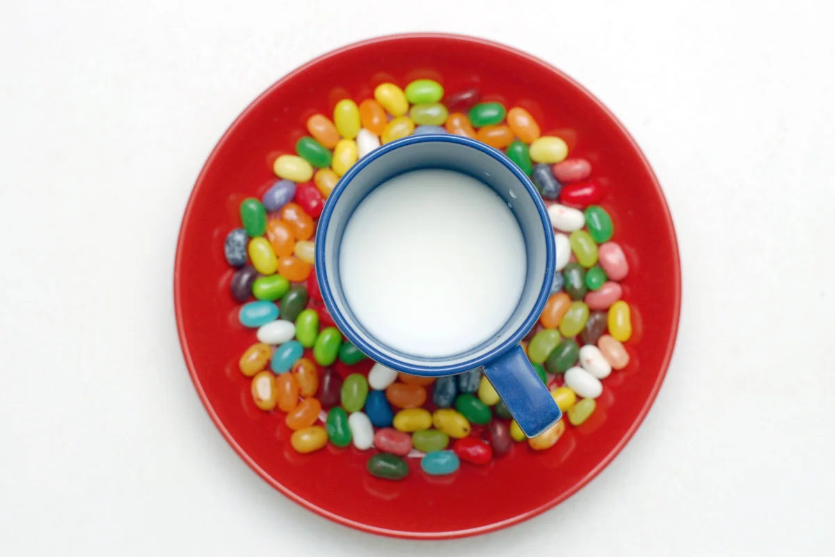 Blue cup of milk on the red plate surrounded by jelly beans