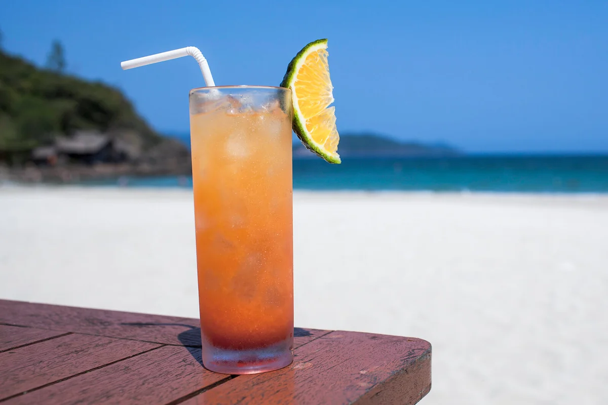 Glass of refreshment on wooden table at beach during sunny day