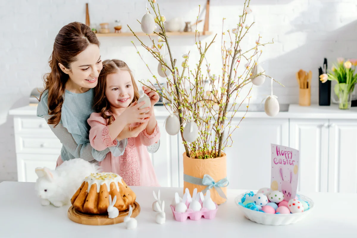 Happy kid touching decorative easter egg on willow branch near mother