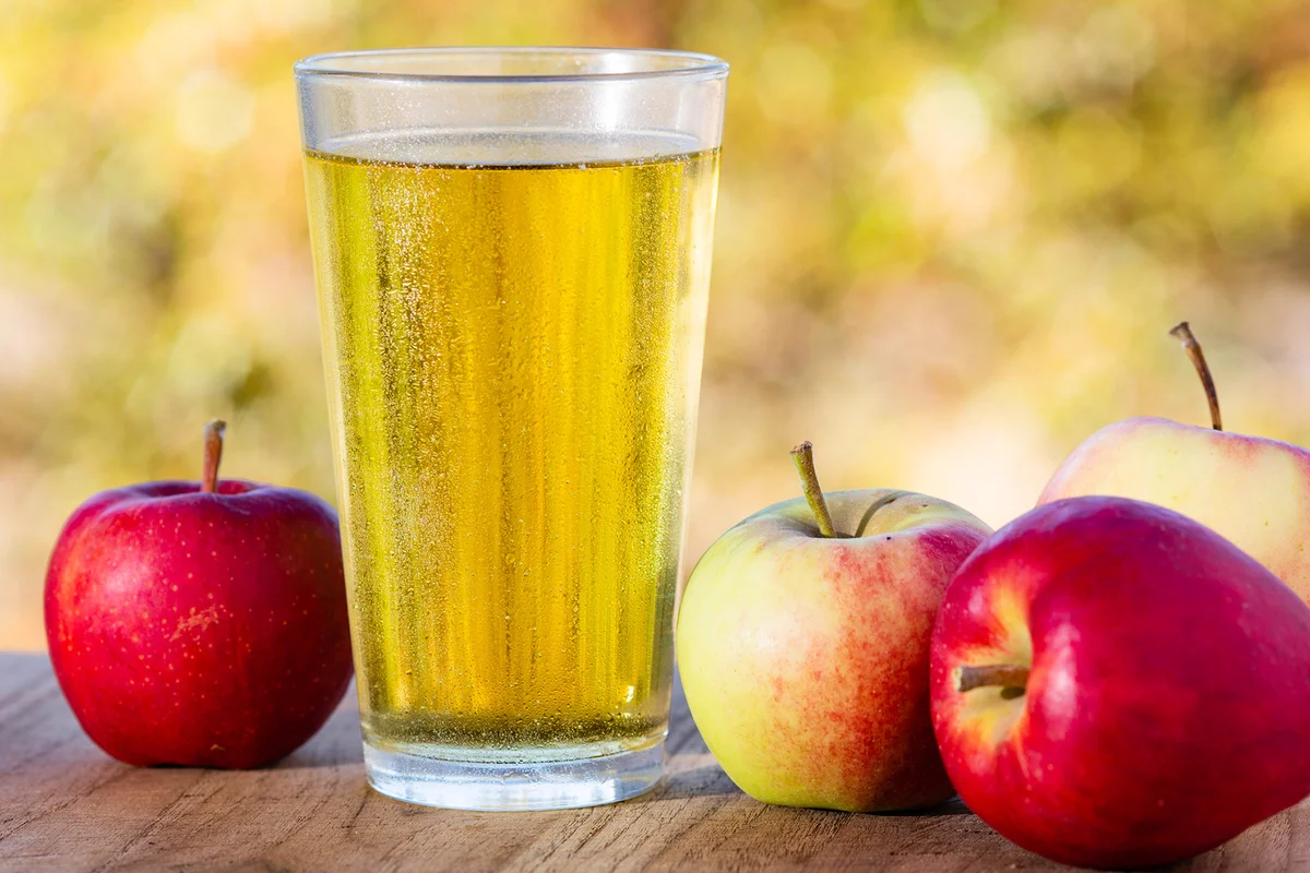 Glass of cider on outdoor table with apples