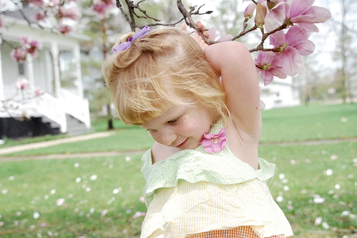 A beautiful young girl holds unto a tulip tree branch covered in pink and white flowers