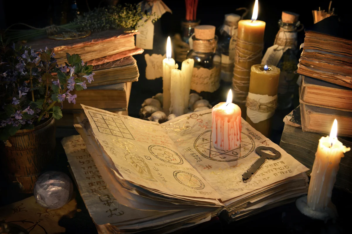 Bloody candle with rustic key on witch book in candle light