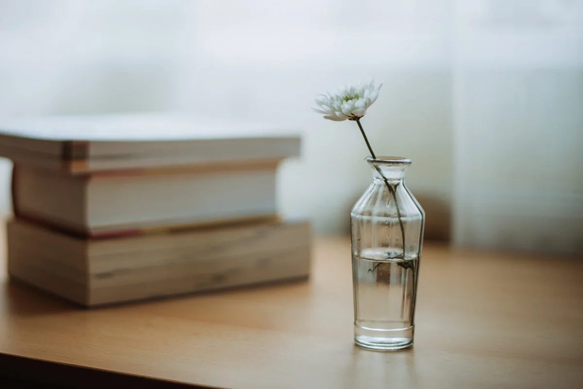 A white flower in a glass vase next to a stack of books