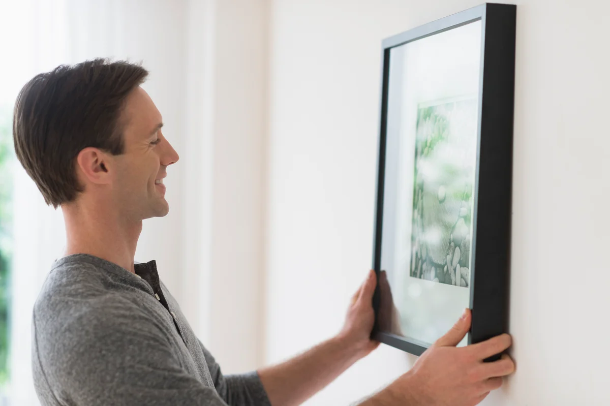 man hanging framed artwork on wall