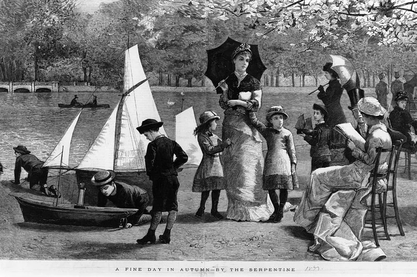 Little boys play with boats and a family takes a stroll by the Serpentine on a sunny Autumn day
