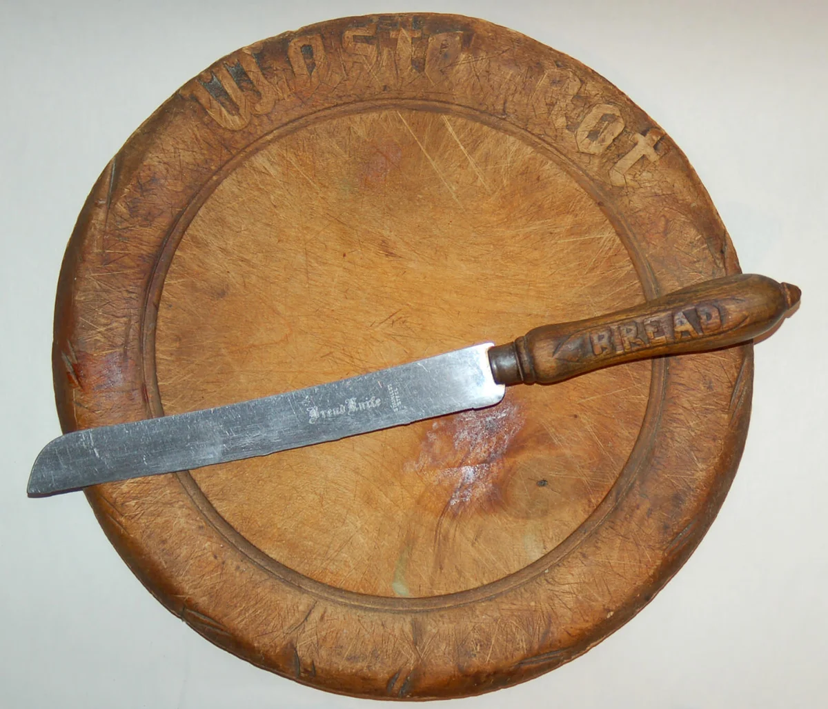 Late 19th century cutting board of maple bearing the admonition "Waste Not" [Want Not] with a bread knife of the same period.