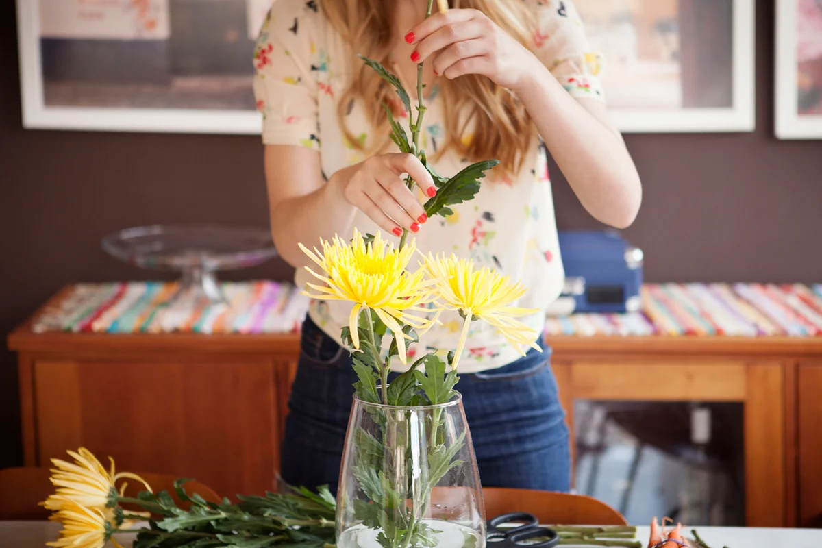 Midsection of woman decorating vase with Chrysanthemums at home