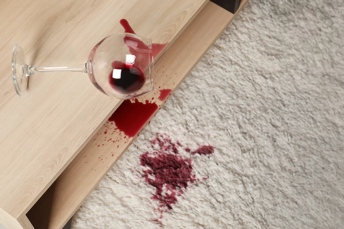 Overturned glass and spilled red wine on white carpet