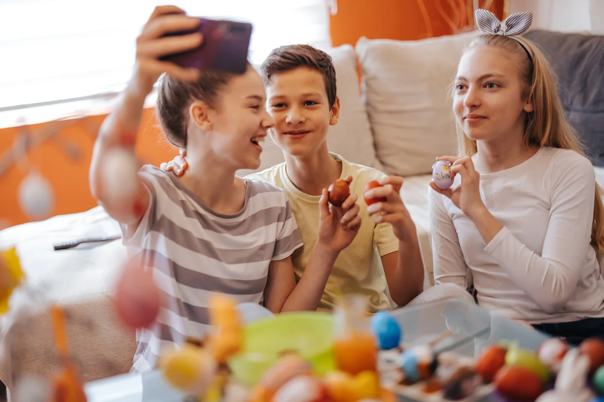 Teenagers holding colorful Easter eggs and taking selfie on mobile phone