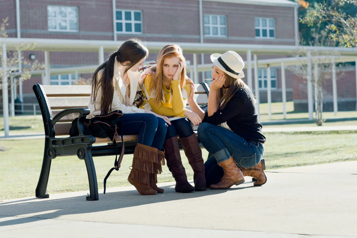 Depressed teenage girl talking to friends at school