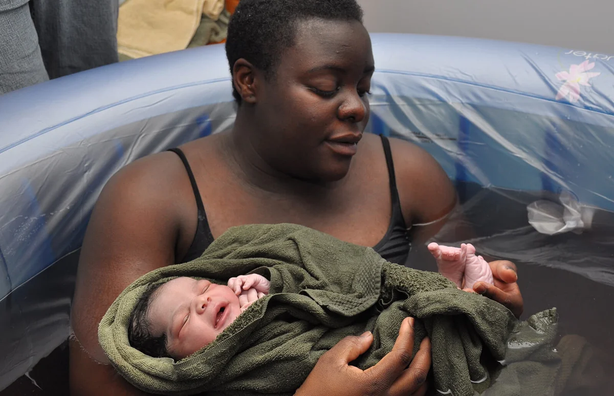mother in birthing tub examines newborn's feet