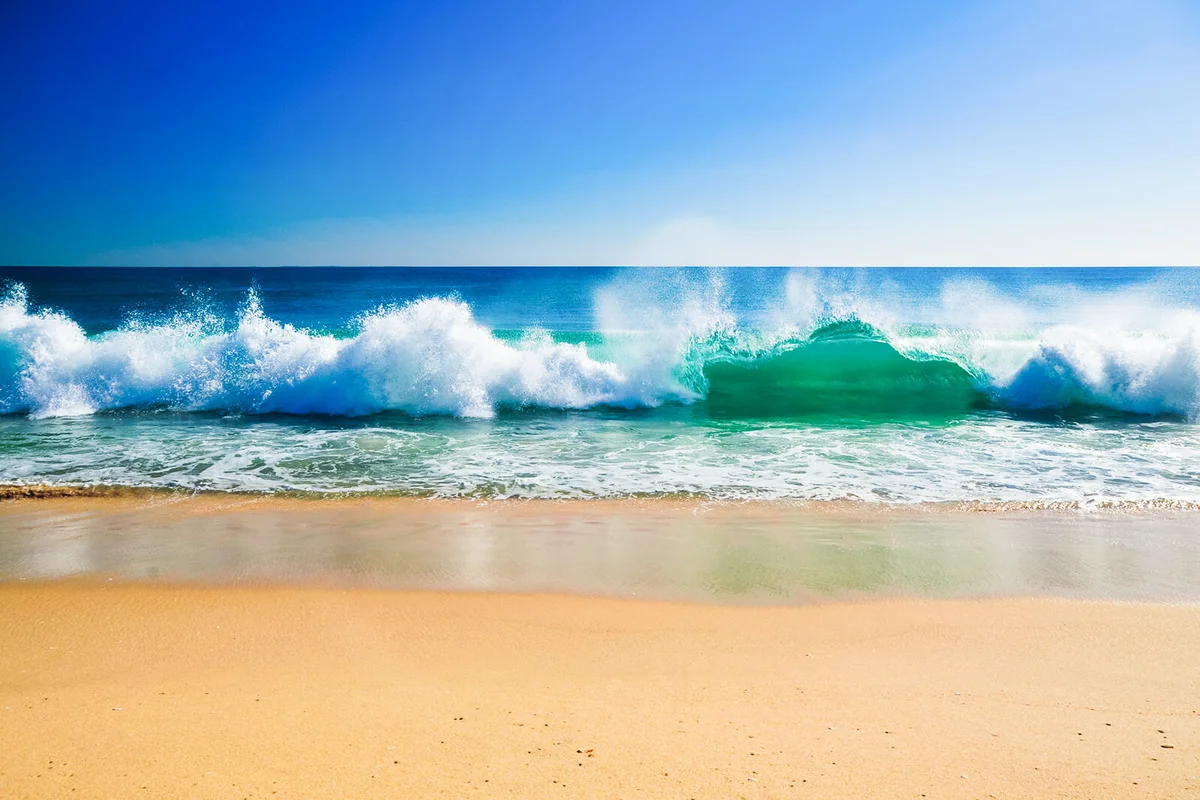 View of beach with sand in front and waves with surf