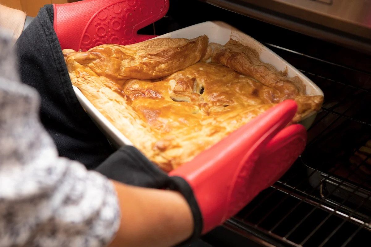 Hands removing a cooked savoury pie from a domestic oven