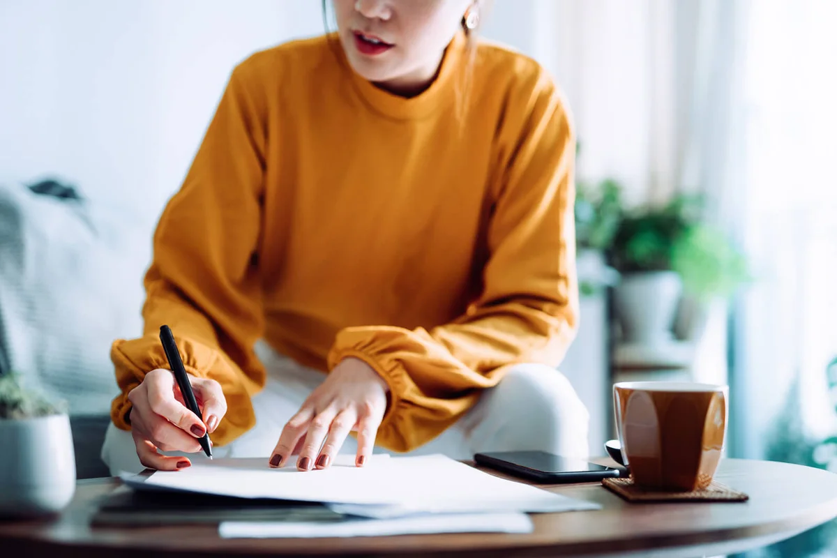 woman holding a pen and signing paperwork in the living room at home