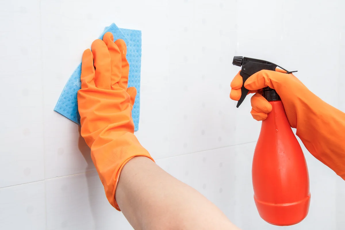 Female hands in orange rubber gloves holds bottle of detergent